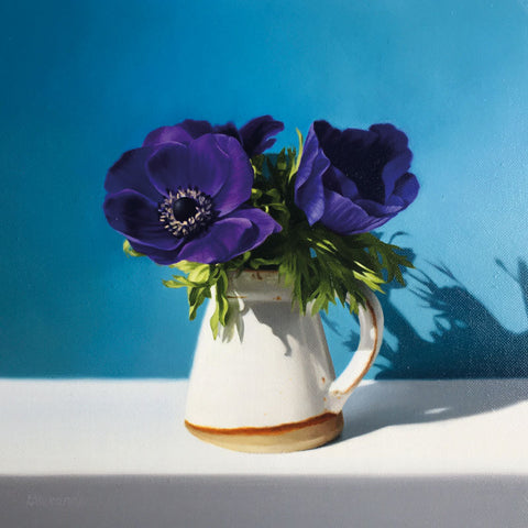 Small ceramic jug with purple anemones on a white table with a blue background.