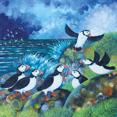 Art greeting card by Lisa Graa Jensen. A group of Puffins on some rocks with the sea and seabirds behind. Cloudy blue sky.