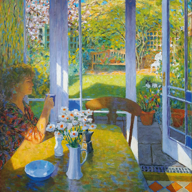 Art greeting card by Patrick Cullen. Woman sitting at a kitchen table, drinking tea in a conservatory with spring flowers in a vase and a sunny view of the garden with a dog.