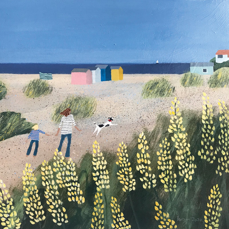 Mother and child with a dog on a beach with beach huts and big yellow flowers in foreground.