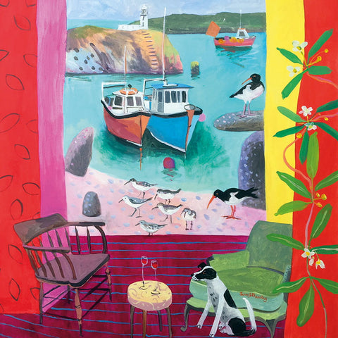 Black and white dog sitting by a table and chairs with two glasses of red wine on the table. Out of the window is a  bay with boats and a group of Sandpipers on the sand.