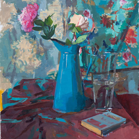 Pink and white Peonies in a tall blue jug on a table with purple table cloth and book.